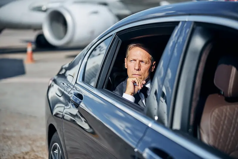 A businessman setting in the backseat of a black car leaving the airport tramac, symbolizing george bush airport transfer.